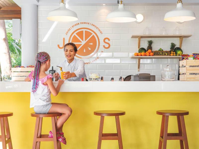 Zwei Frauen im Gespräch an einer sonnengelben Bar in einem hellen, modernen Café.