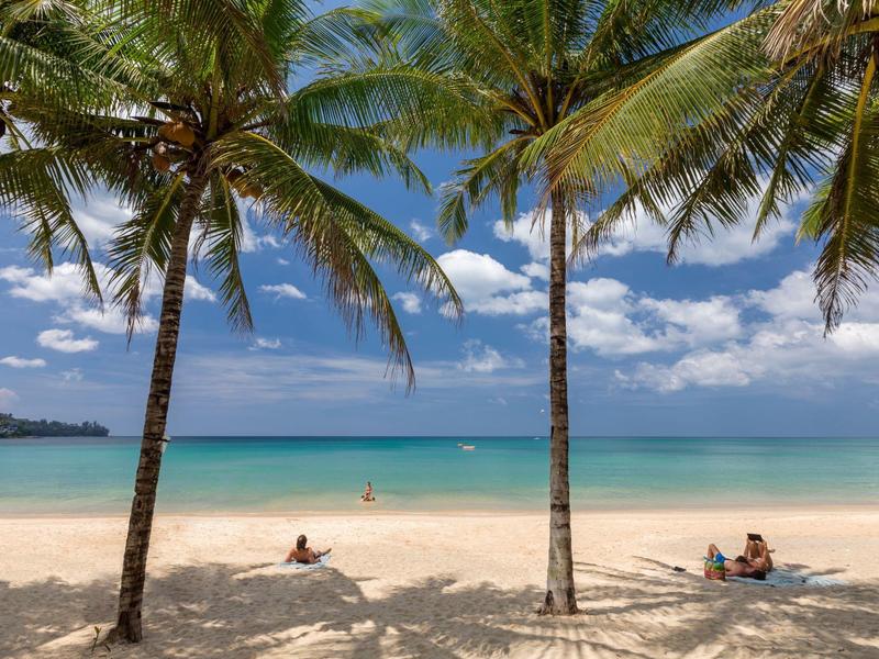 Strand mit weißen Sand, Palmen und blauem Himmel mit Wolken am Meer
