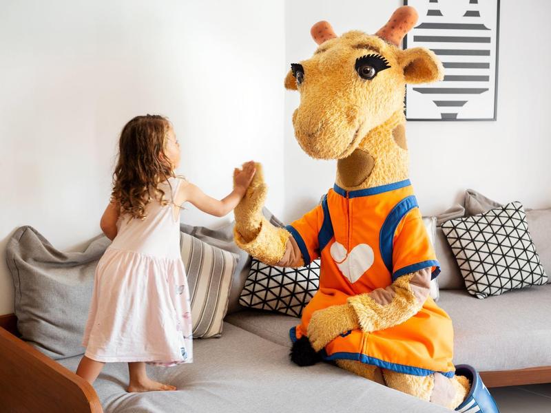 Kind gibt einer Person in einem niedlichen Giraffenkostüm in einem Wohnzimmer die Hand.