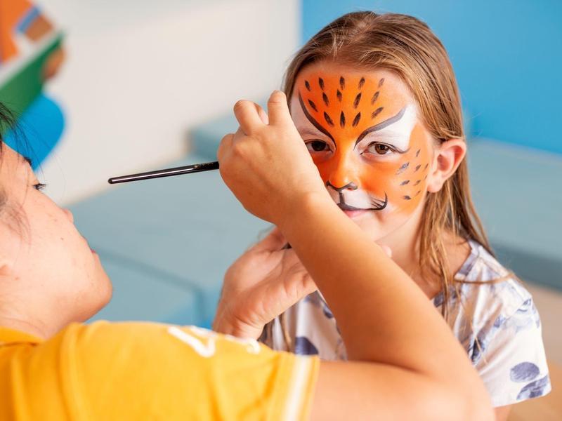 Kind erhält eine Gesichtsmaske mit Tiger-Motiv in einer Freizeiteinrichtung.