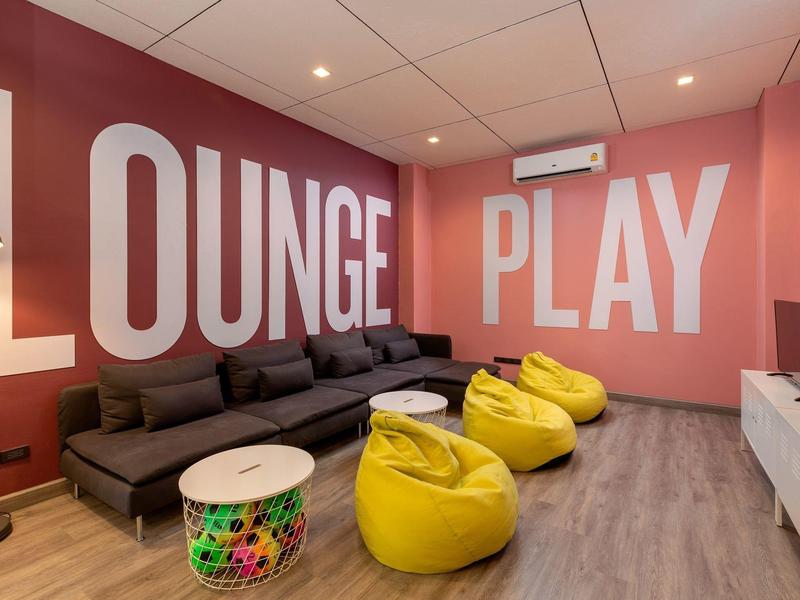 Gemütlicher Spiel- und Loungebereich mit gelben Sitzsäcken, Sofa und TV in einem Hotel.