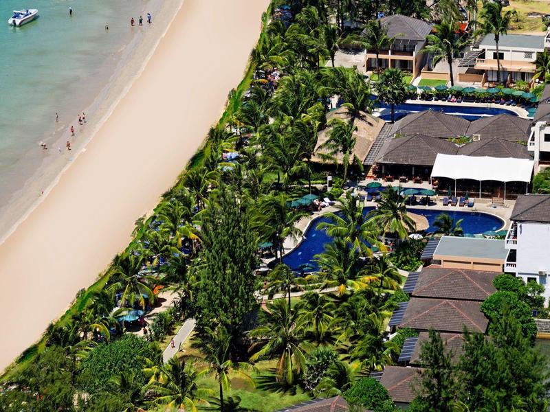 Vogelperspektive eines tropischen Strandes mit Resort, Pool und Palmen entlang des Sandstrandes.