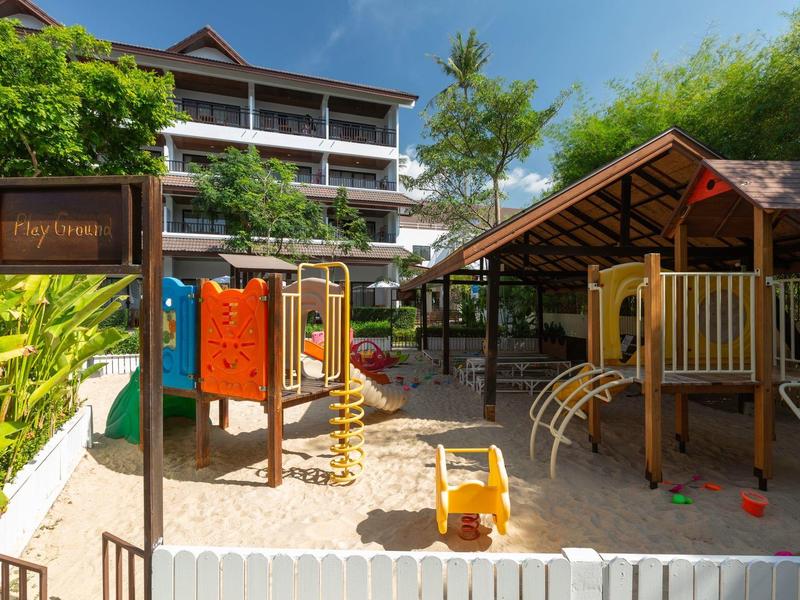 Kinderspielplatz mit Sandfläche und Klettergeräten vor einem mehrstöckigen Hotelgebäude