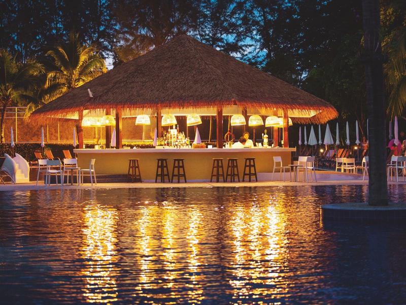 Beleuchtete Bar mit Strohdach am Pool in tropischer Umgebung bei Nacht