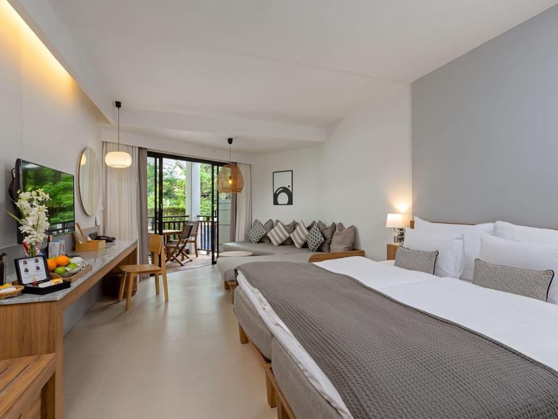 Modernes Hotelzimmer mit großem Bett, Schreibtisch, TV und Balkon mit Blick auf Grünflächen.