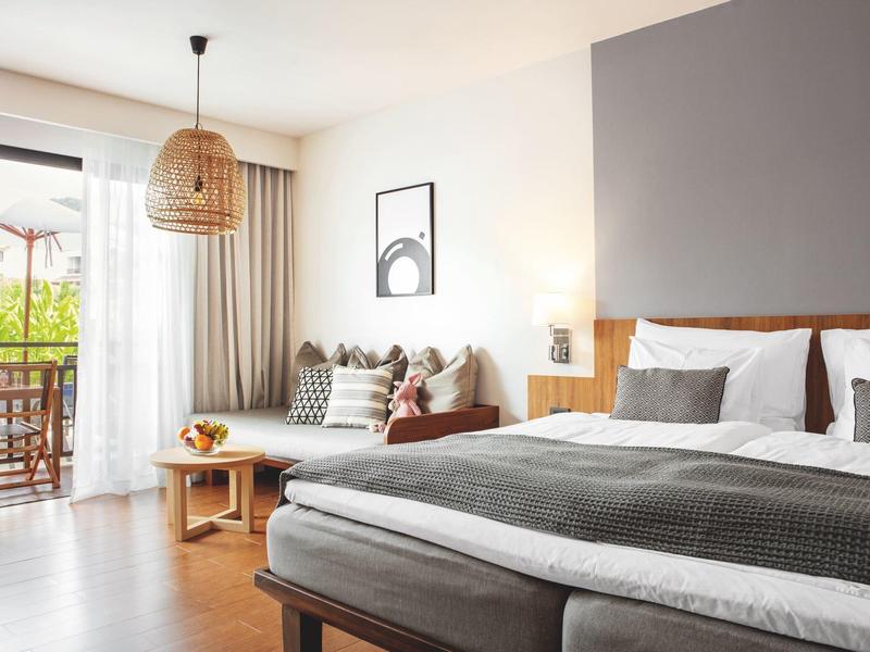 Modern eingerichtetes Hotelzimmer mit großem Bett, Sofa und Balkon mit Holzmöbeln.