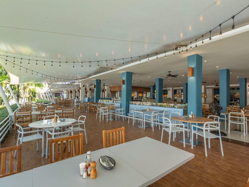 Große, offene Terrasse mit Holzfußboden, vielen weißen Tischen und Stühlen unter einem weißen Dach.