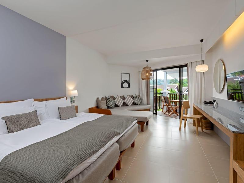 Modernes Hotelzimmer mit zwei Betten, Sitzbereich und Balkon mit Blick ins Freie.