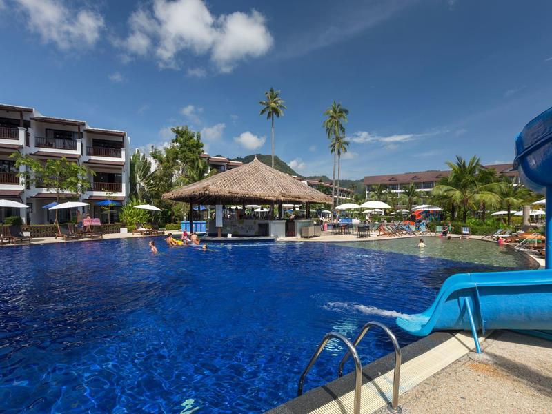 Ein großer Pool mit blauen Rutschen und einem Strohdachbar im Hintergrund an einem sonnigen Tag.