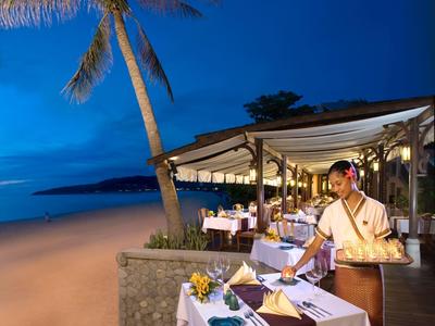 Ein Restaurant am Strand bei Abenddämmerung, mit gedeckten Tischen und einer Kellnerin im traditionellen Kleid.