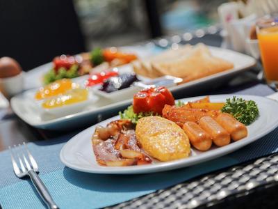 Ein Frühstücksteller mit Rührei, Würstchen, Speck und Gemüse, dazu eine weitere Frühstücksplatte.