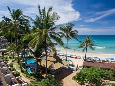 Strand mit Palmen, Liegestühlen, blauem Meer und klarem Himmel neben Hotelbalkonen.