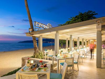 Strandrestaurant bei Sonnenuntergang mit gedeckten Tischen und Blick auf das ruhige Meer.