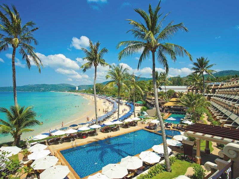 Strandresort mit Pool, Palmen und Sonnenschirmen entlang türkisfarbenem Meer unter blauem Himmel.