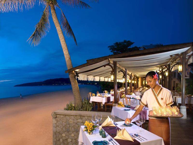 Ein Restaurant am Strand bei Abenddämmerung, mit gedeckten Tischen und einer Kellnerin im traditionellen Kleid.