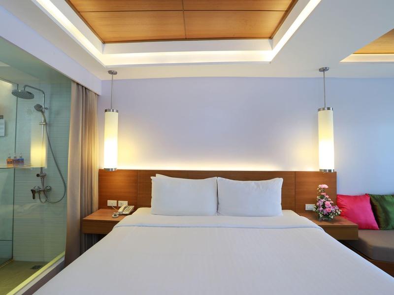 Modernes Schlafzimmer mit großem weißem Bett, Holzwand, farbigen Kissen und Glasdusche.