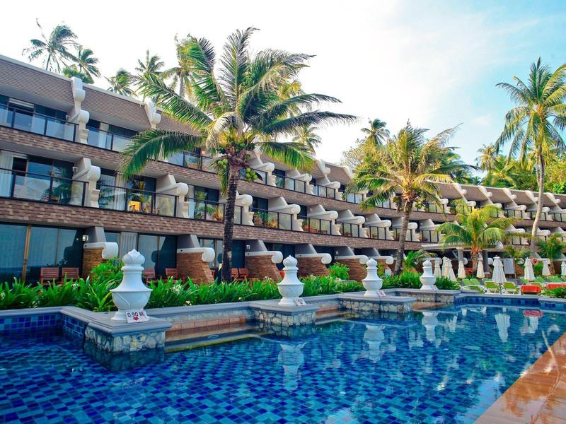 Ein großes Hotelgebäude mit mehreren Balkonen vor einem blauen Pool und Palmen.
