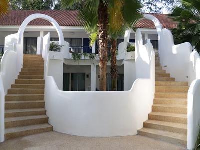 Weiße doppelte Treppe mit geschwungenen Geländern vor einem Gebäude und Palmen im Hintergrund.
