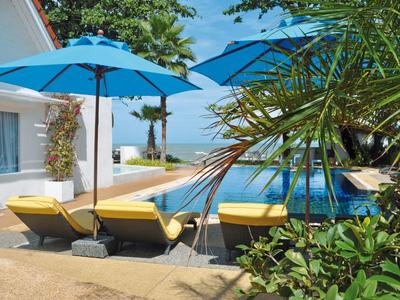 Drei gelbe Liegestühle unter blauen Sonnenschirmen neben einem Pool mit Palmen und blauem Himmel.