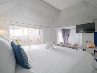 Helles Schlafzimmer mit weißer Decke, großem Bett, blauen Kissen und hellem Holzmöbeln.