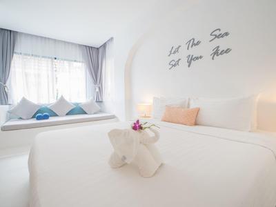 Helles Schlafzimmer mit großem Bett, bunten Kissen und Fensterbank mit Sitzkissen und Vorhängen.