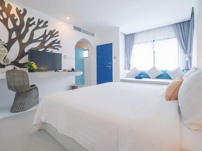 Helles Schlafzimmer mit weißer Einrichtung, blauer Tür, Fensterbank und Baum-Wanddekor links.