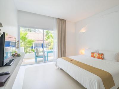 Helles Schlafzimmer mit Doppelbett, Fernseher, weißen Wänden und Blick auf Terrasse mit Stühlen.