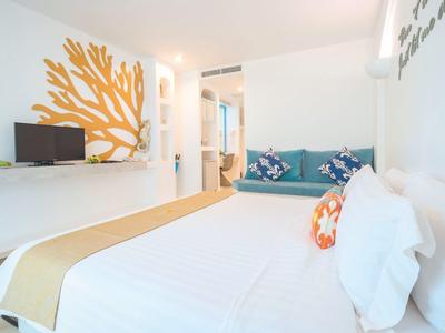 Hell eingerichtetes Schlafzimmer mit weißem Bett, blauer Couch und dekorativem Korallenmotiv an der Wand.