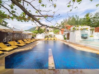 Großes blauer Pool mit gelben Liegestühlen, grünen Pflanzen und weißem Gebäude im Hintergrund.