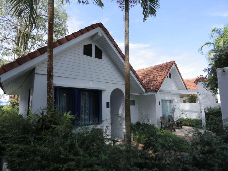 Kleine weiße Häuser mit roten Dächern und Palmen in einer tropischen Umgebung.