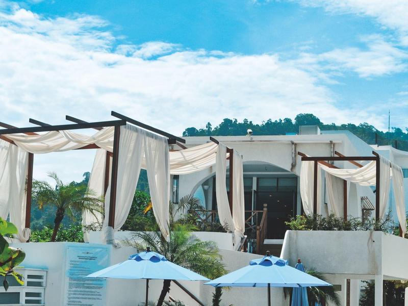 Moderne weiße Hotelterrasse mit Pavillons und blauen Sonnenschirmen unter blauem Himmel.