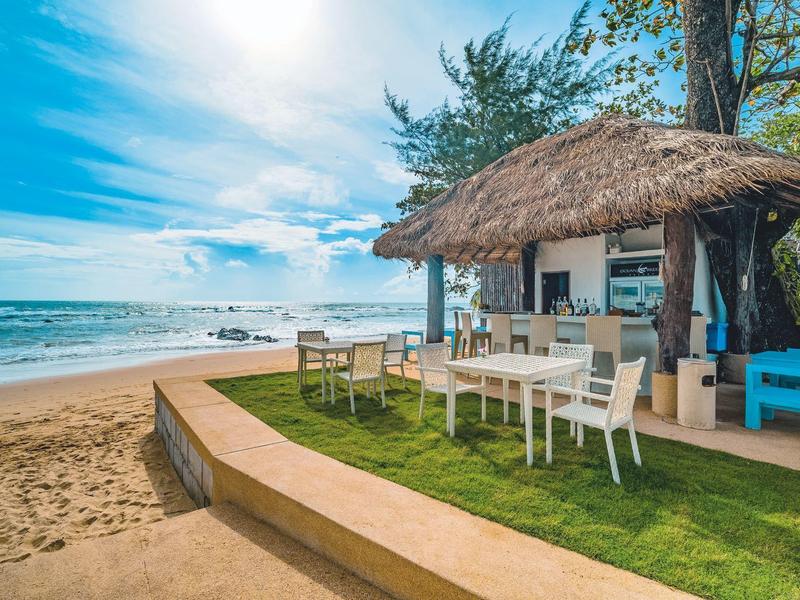 Strandbar mit Strohdach, Tischen und Stühlen neben dem Meer bei sonnigem Himmel