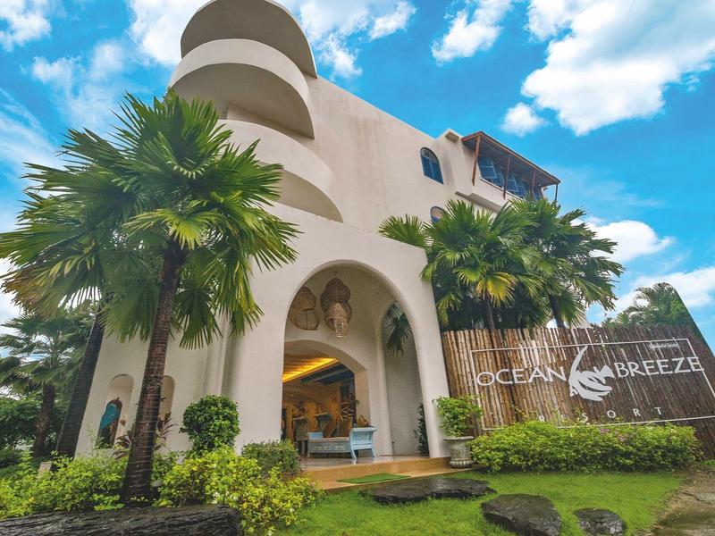 Modernes Hotel mit Palmen, großen Bögen und blauem Himmel.