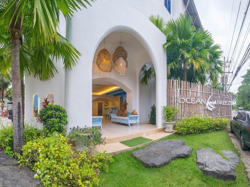 Eingang eines Hotels mit weißer Fassade, Palmen und grüner Landschaft.