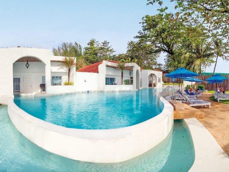 Runder Pool mit Blick auf das Meer, umgeben von Bäumen und weißem Mobiliar.