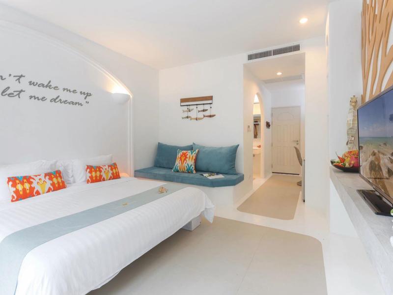 Modernes, helles Hotelzimmer mit Doppelbett, Wandzitaten und Sitzbereich in Weiß- und Blautönen.