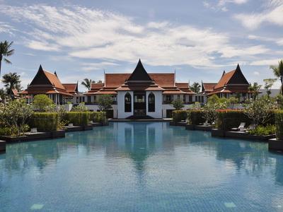 Un resort spazioso con una grande piscina e edifici di ispirazione asiatica sotto un cielo nuvoloso.