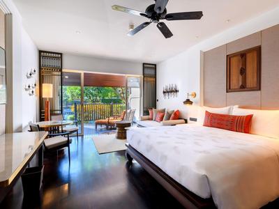 Helles Hotelzimmer mit großem Bett, modernem Mobiliar und Zugang zu einer Terrasse mit Gartenblick.