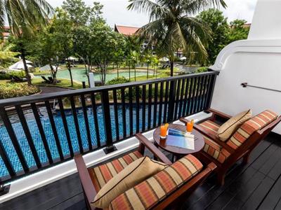 Balkon mit zwei Liegestühlen, kleinem Tisch und Blick auf Pool und Palmen in tropischer Umgebung.