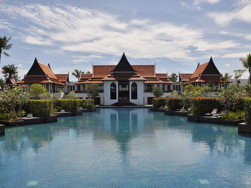 Großer Pool mit Blick auf ein traditionelles Resort unter bewölktem Himmel