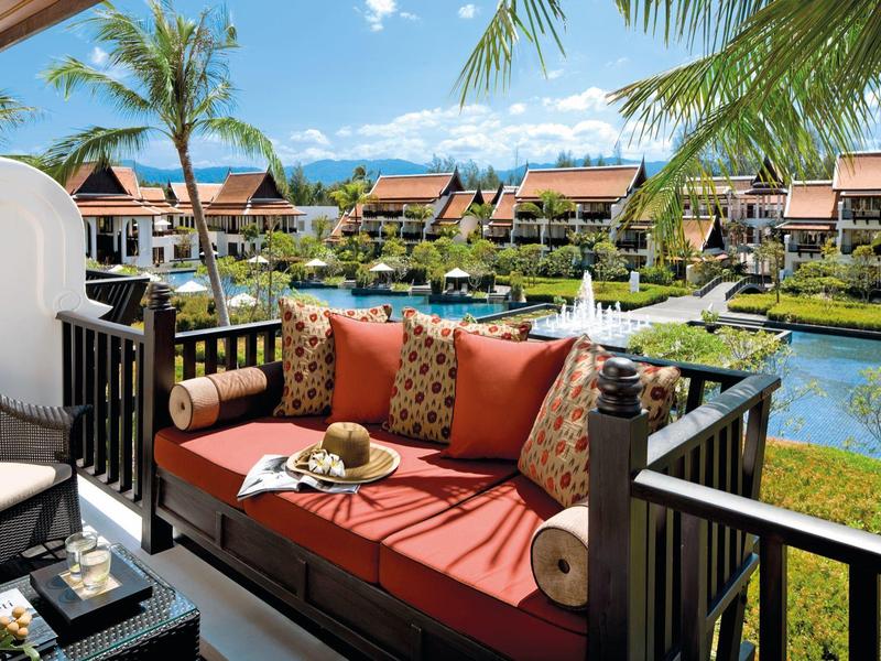 Balkon mit rotem Sofa und Blick auf tropische Gartenanlage mit Pool und Villen.