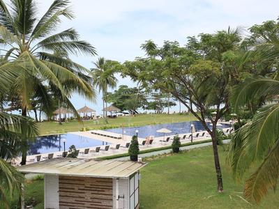 Blick auf einen Swimmingpool und Liegestühle mit Palmen im Vordergrund am Hotelstrand.