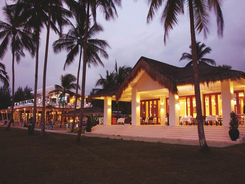 Leuchtendes Haus mit Terrasse, umgeben von Palmen, bei Abenddämmerung, entspannte Atmosphäre.