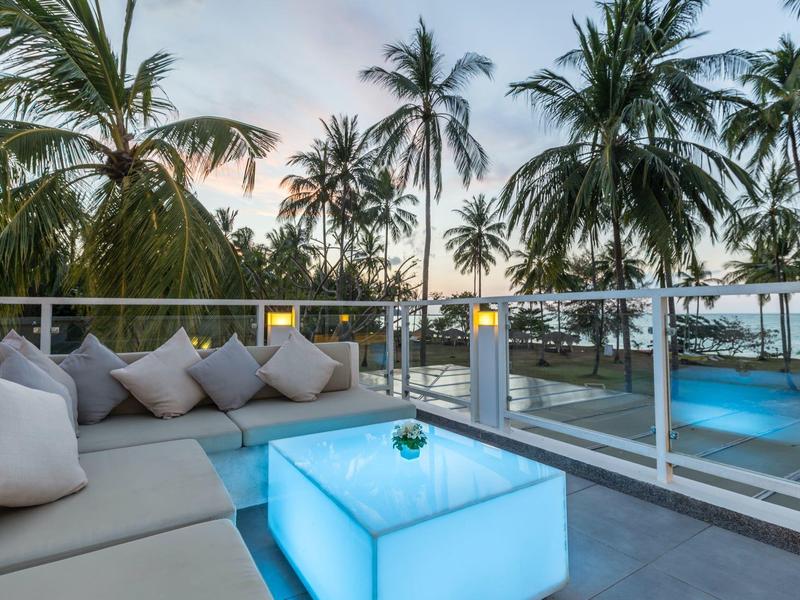 Moderne Außenterrasse mit bläulich beleuchtetem Tisch, grauem Sofa und Palmen im Hintergrund bei Sonnenuntergang.