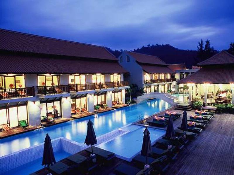 Luxuriöses Hotel mit großem beleuchtetem Pool, Liegestühlen und dunklem Abendhimmel.