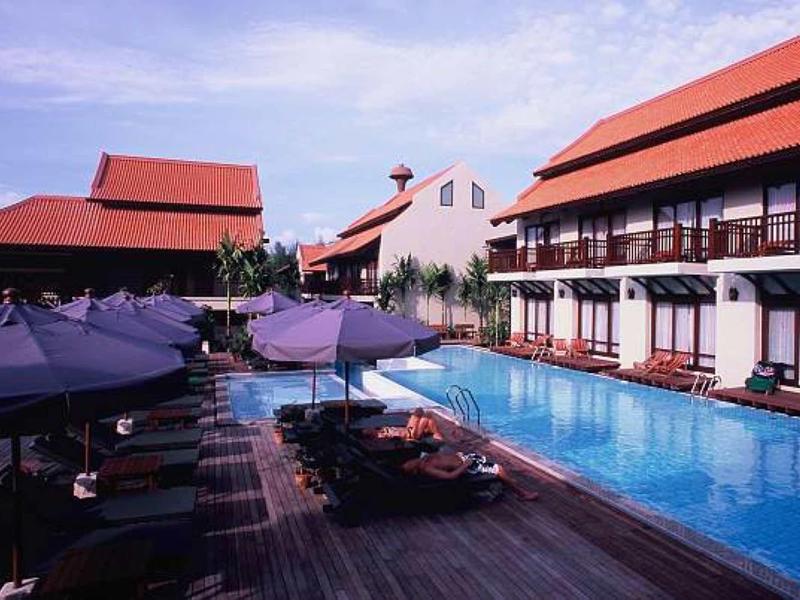 Hotel mit großem Pool, Sonnenschirmen, roten Dächern und Holzboden bei klarem Himmel.