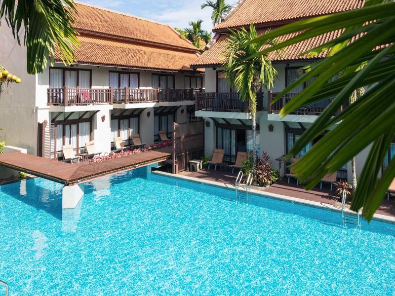 Großer blauer Pool mit umgebenden tropischen Pflanzen und Gebäuden mit roten Dächern.