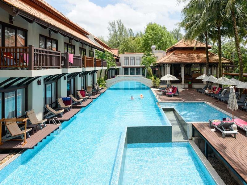 Freizeitbereich mit langem blauen Pool, Liegestühlen, Holzterrasse und umliegenden Gebäuden.