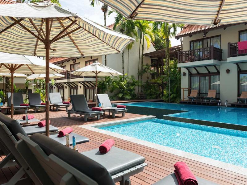 Moderner Außenpool mit Liegestühlen und Sonnenschirmen neben einem mehrstöckigen Hotelgebäude.