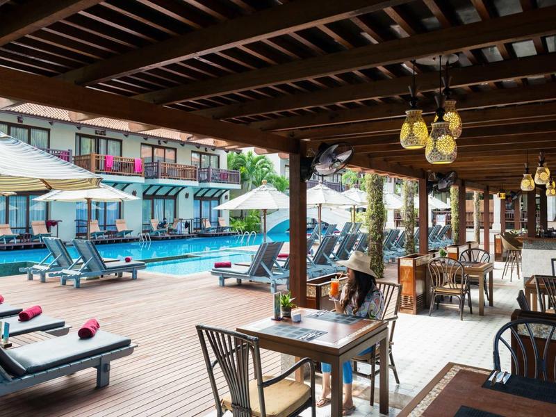 Freiluftrestaurant mit Holzdach neben Schwimmbad, Tisch- und Liegestühle, helle Beleuchtung.